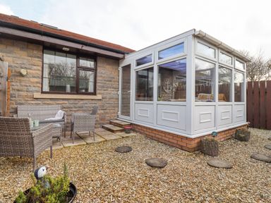 A garden area with stone gravel floor and outdoor seating next to a conservatory at The Bolthole (Seahouses) in Seahouses