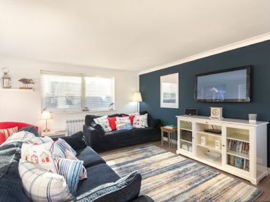 A living room with sofas and a television on a stand at Stones Throw in Beadnell