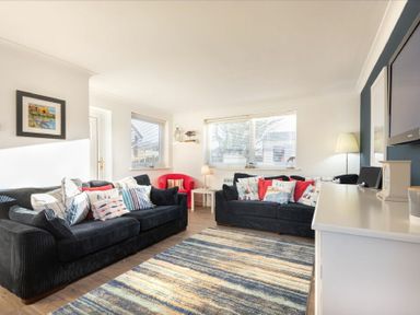 A living room with two black sofas and a red armchair with cushions a striped rug and a television at Stones Throw in Beadnell