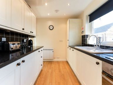 A kitchen with white cabinets black countertops a toaster kettle and a sink at Stones Throw in Beadnell