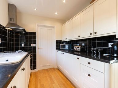 A kitchen with white cabinets black countertops and black tiled backsplash at Stones Throw in Beadnell