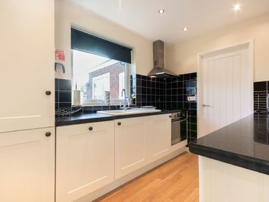 A kitchen with white cabinets black countertops black tiled backsplash and a window at Stones Throw Beadnell