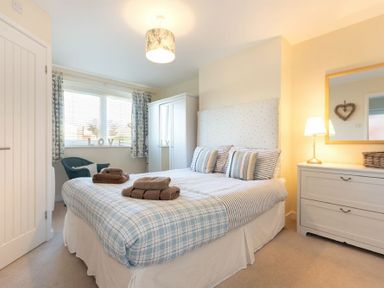 A bedroom with a bed pillows and folded towels next to a wardrobe and a dresser with a lamp at Stones Throw in Beadnell