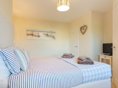 A bedroom with a bed with striped bedding a wall painting towels on the bed and a television on a small table at Stones Throw in Beadnell