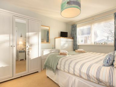 A bedroom with a bed linens striped next to a window with blinds and curtains at Stones Throw in Beadnell