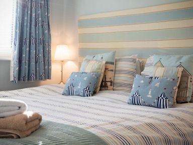A bedroom with a bed featuring striped bedding and multiple pillows with nautical patterns and a lamp next to a window with matching curtains at Stones Throw in Beadnell