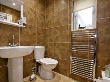 A bathroom with a sink a toilet a metal towel rack and a small window at Stones Throw in Beadnell