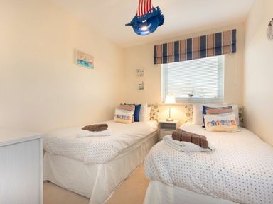 A bedroom with two single beds a nightstand and a window with striped curtains at Stones Throw in Beadnell