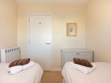 A bedroom with two single beds a white door and a wooden dresser at Stones Throw in Beadnell