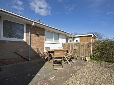 An outdoor patio area with a wooden table and six wooden chairs next to a brick and white wall at Stones Throw in Beadnell