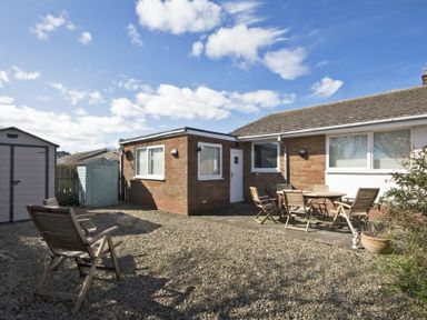 A backyard with gravel ground wooden chairs and table near a brick house at Stones Throw in Beadnell