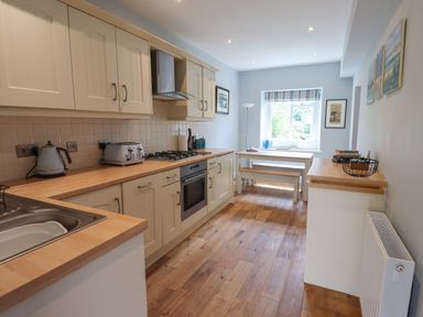 A kitchen with wooden countertops a sink a kettle a toaster and a stove with oven and a dining table with benches by a window at Alnside Cottage in Alnmouth