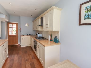 A kitchen with wooden floor cabinets and countertop a stove oven and a clock on the wall at Alnside Cottage in Alnmouth