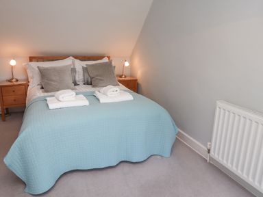 A bedroom with a double bed with folded towels bedside tables with lamps and a radiator on the wall at Alnside Cottage in Alnmouth