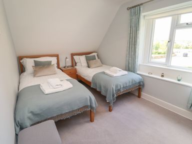 A bedroom with two single beds a nightstand a window and light blue curtains at Alnside Cottage in Alnmouth