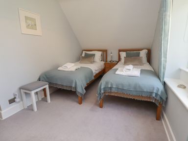 A bedroom with two single beds a small wooden nightstand between them and a small stool at Alnside Cottage in Alnmouth