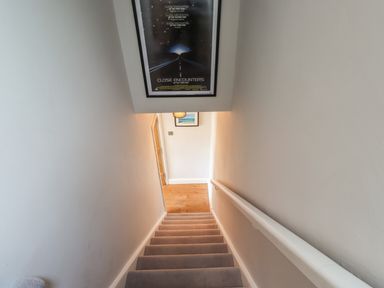 A carpeted staircase with a handrail leading to a wooden floor and framed artwork on the walls at Alnside Cottage in Alnmouth