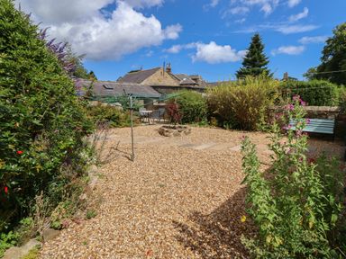 A garden with gravel ground a fire pit a drying rack outdoor table and chairs surrounded by shrubs and flowers at Alnside Cottage in Alnmouth