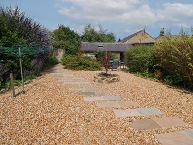 A garden with a gravel path and stepping stones leading to a small stone building surrounded by bushes at Alnside Cottage in Alnmouth