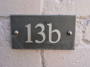 A black house number plaque with 13b attached to a textured light-colored wall at Riverside Lodge in Alnmouth