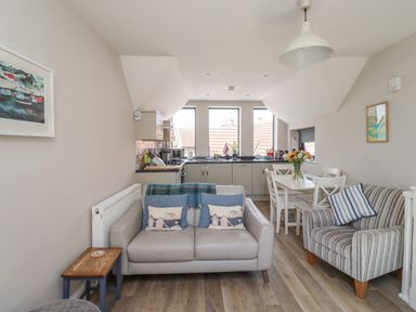 A kitchen and living area with a sofa, armchair, dining table, and flower vase at Riverside Lodge in Alnmouth