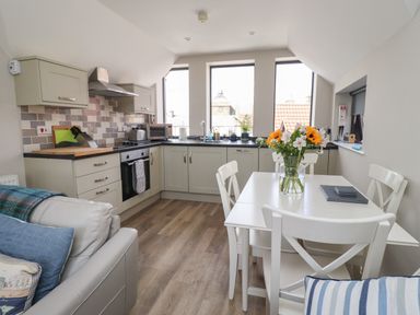 A kitchen and dining area with cabinets appliances a table with flowers and chairs at Riverside Lodge in Alnmouth