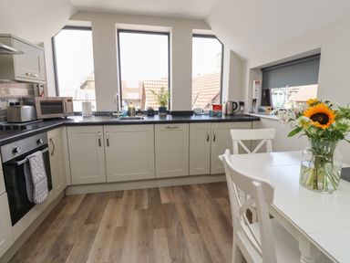 A kitchen with white cabinets and a table with chairs and a vase of flowers at Riverside Lodge in Alnmouth