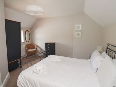 A bedroom with a bed with white sheets two black dressers a wicker chair and a round mirror at Riverside Lodge in Alnmouth