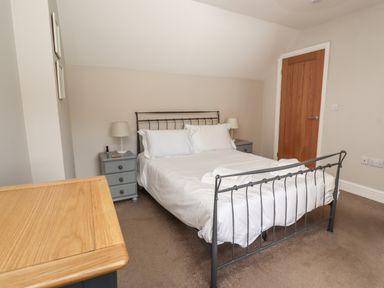 A bedroom with a metal frame bed two bedside tables with lamps a wooden dresser and a wooden door at Riverside Lodge in Alnmouth