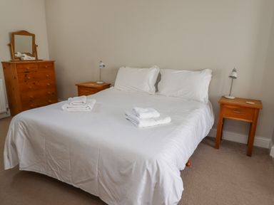 A bedroom with a bed with white linens two wooden bedside tables and a wooden dresser with a mirror at Riverside Lodge in Alnmouth