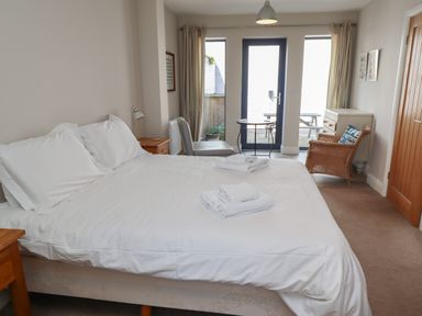 A bedroom with a white bed and folded towels a wicker chair and a chest of drawers at Riverside Lodge in Alnmouth