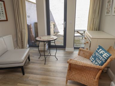 A small sitting area with a wicker chair and cushion a white chest of drawers a round mosaic table and a white leather chair at Riverside Lodge in Alnmouth