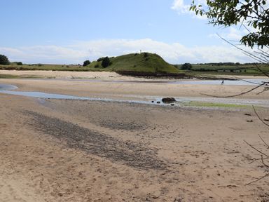 A sandy beach with a grassy hill and a cross in the distance at Riverside Lodge in Alnmouth