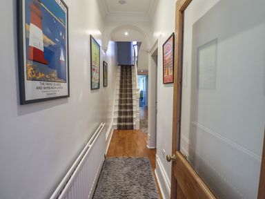 A hallway with framed artwork on the walls a striped carpeted staircase and a wooden floor at Number Seventeen in Amble