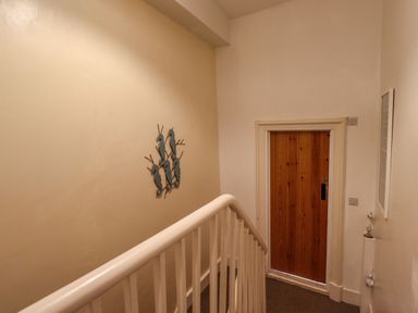 A staircase landing with white railing a wooden door and seahorse wall decoration at Number Seventeen in Amble