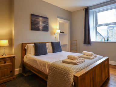 A bedroom with a wooden bed and side table beside a window at Number Seventeen in Amble