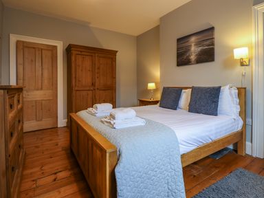 A bedroom with a wooden bed and furniture and a photograph on the wall at Number Seventeen in Amble
