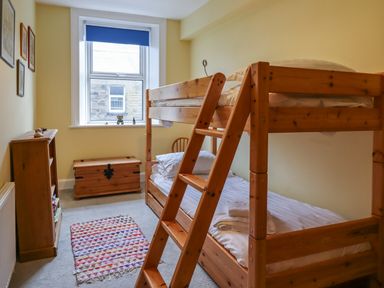A bedroom with wooden bunk beds a small wooden bookshelf a wooden chest and a window at Number Seventeen in Amble