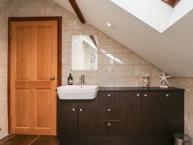 A bathroom with a wooden door dark brown cabinets a white sink and a mirror at Number Seventeen in Amble