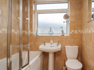A bathroom with a bathtub and glass shower screen a pedestal sink a toilet and a frosted window with decorative items at Number Seventeen in Amble