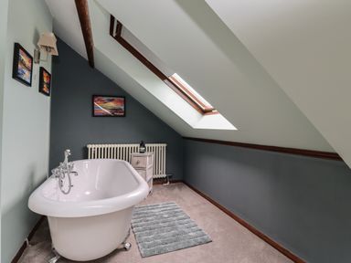 A bathroom with a freestanding bathtub a small cabinet a radiator skylight window and framed pictures on the wall at Number Seventeen in Amble