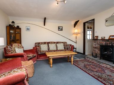 A living room with red velvet sofas a wooden coffee table a brick fireplace and a fishing rod on the wall at Swallows Cottage nr Warkworth in Acklington