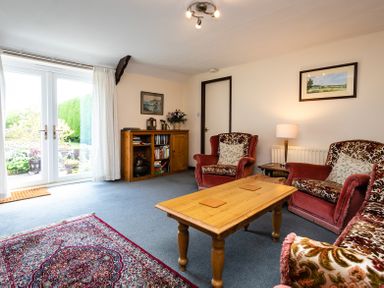 A living room with red patterned armchairs a wooden coffee table a wooden cabinet and French doors at Swallows Cottage nr Warkworth in Acklington
