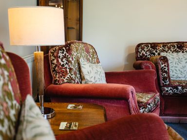 A living room with patterned armchairs a wooden table and a table lamp at Swallows Cottage nr Warkworth in Acklington