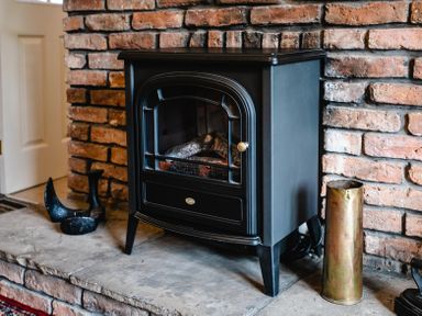 A black wood stove on a stone hearth with a brick wall behind at Swallows Cottage nr Warkworth in Acklington