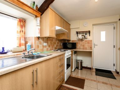 A kitchen with wooden cabinets a sink an oven a microwave and various kitchen utensils at Swallows Cottage nr Warkworth in Acklington