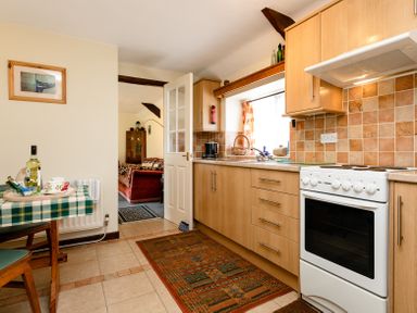A kitchen with wooden cabinets a white oven a tiled backsplash and a small table with a checkered tablecloth at Swallows Cottage nr Warkworth in Acklington