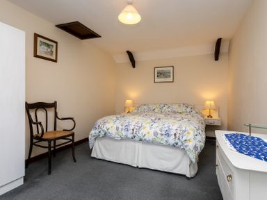 A bedroom with a double bed floral bedding and two lamps on bedside tables with a wooden chair and white dresser at Swallows Cottage nr Warkworth in Acklington