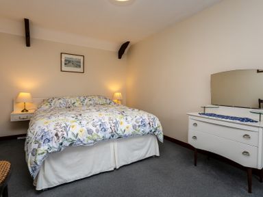 A bedroom with a double bed with floral bedding two bedside lamps a painting on the wall and a white dresser with a mirror at Swallows Cottage nr Warkworth in Acklington