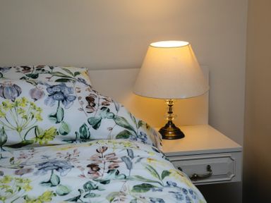 A bed with floral patterned bedding next to a white bedside table with a lamp at Swallows Cottage nr Warkworth in Acklington